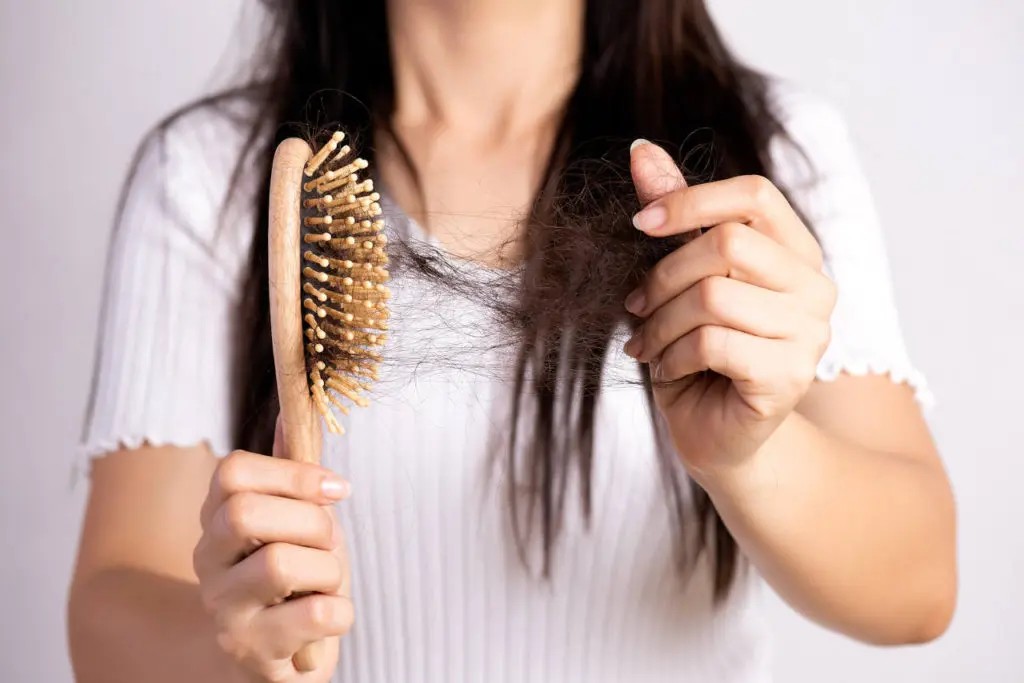 A woman pulls a large clump of hair from a hairbrush.