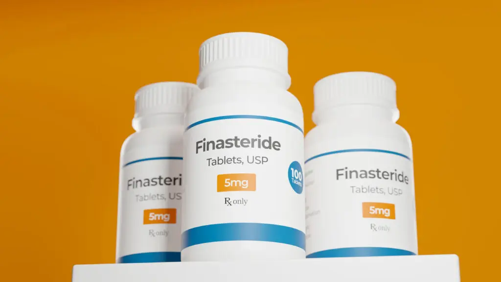 Three bottles of Finasteride against an orange background.
