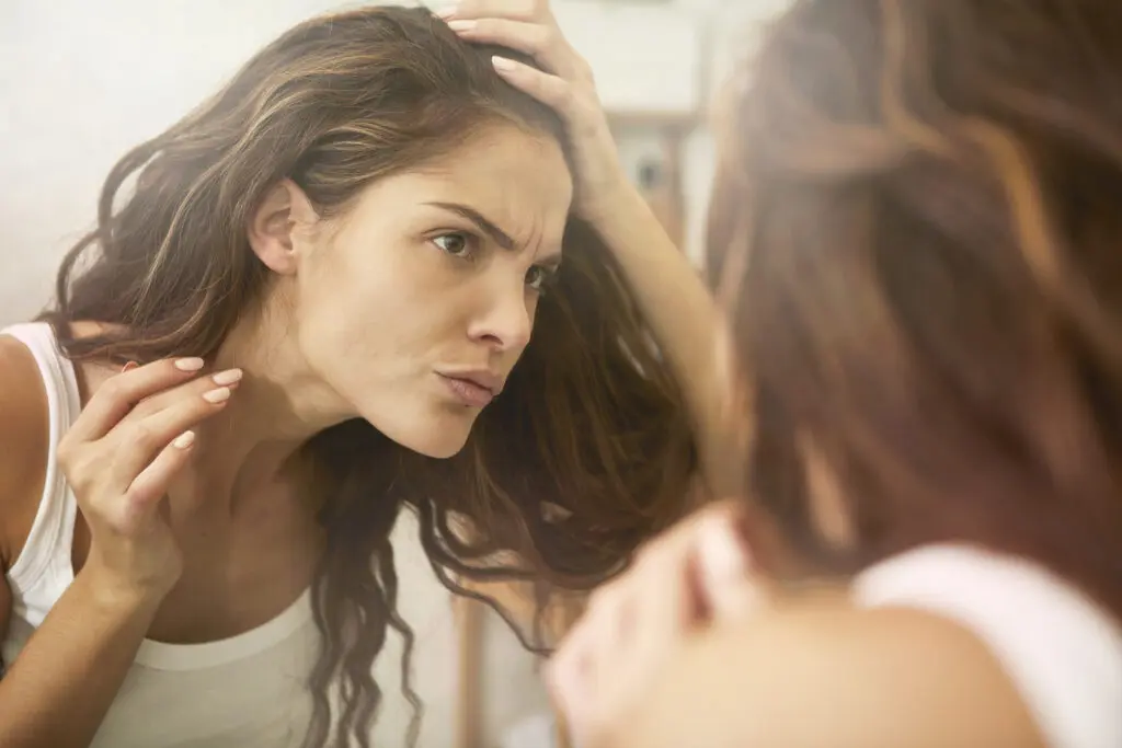 Woman looking in mirror for hair shedding.