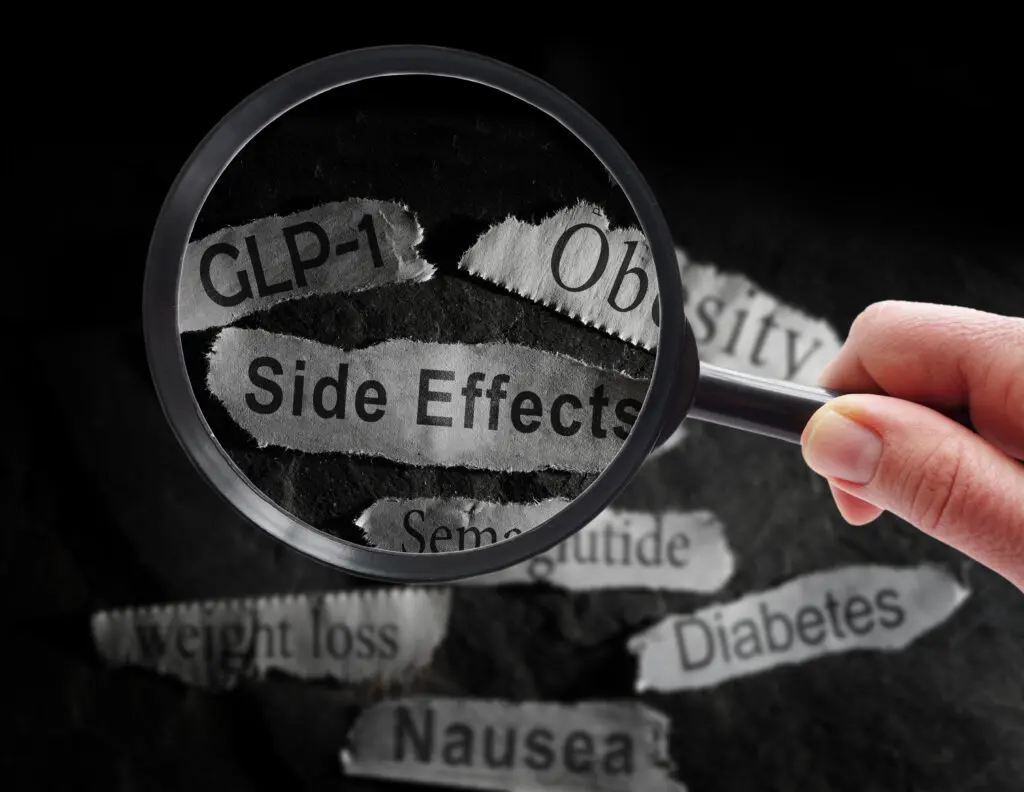 A magnifying glass help over scraps of paper, each listing common side effects of Ozempic.