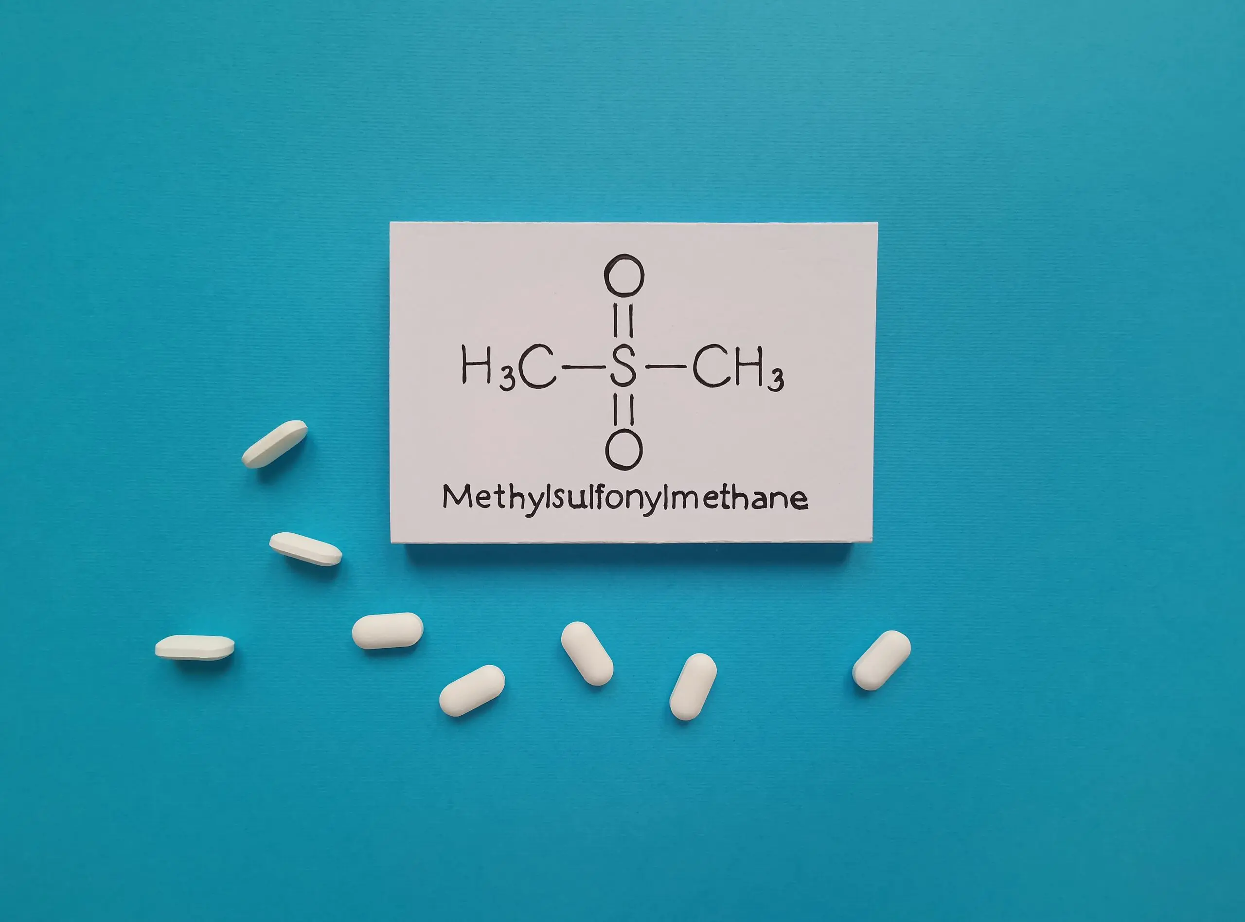 The chemical structure of methylsulfonylmethane surrounded by white MSM pills.