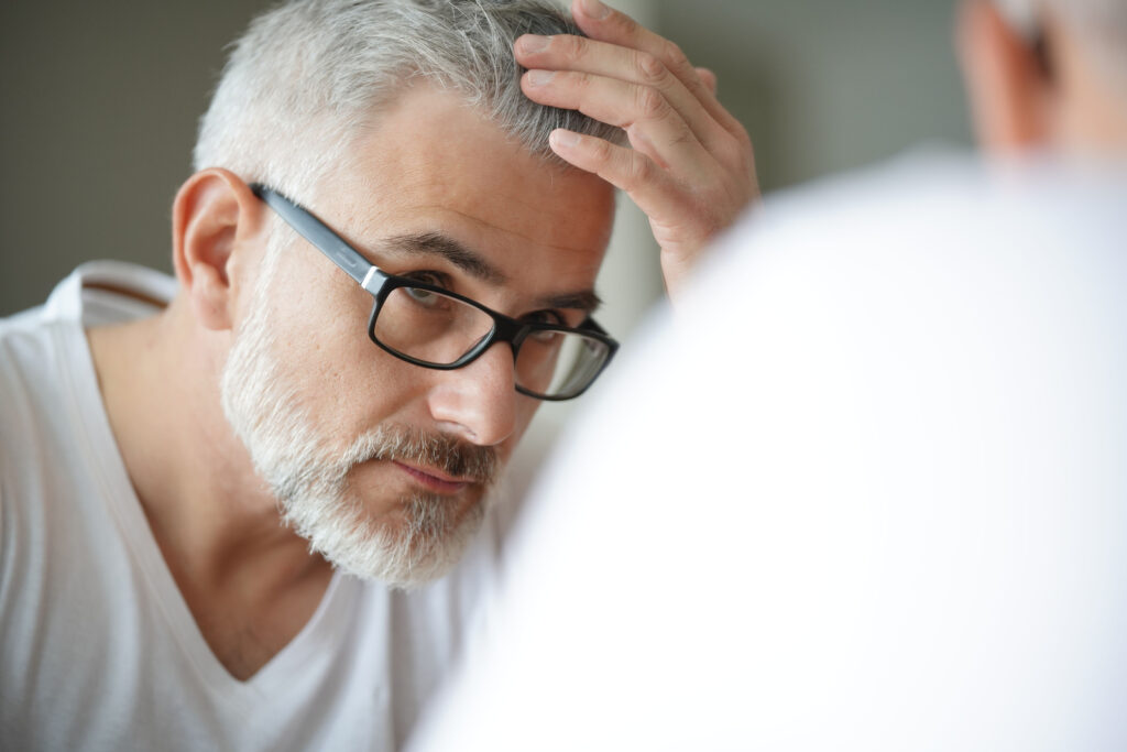 Older man checking hair for hair loss in the mirror