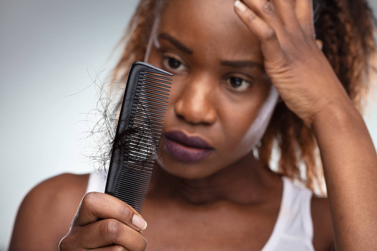 A dismayed woman holds a comb in which a clump of her hair has come loose.