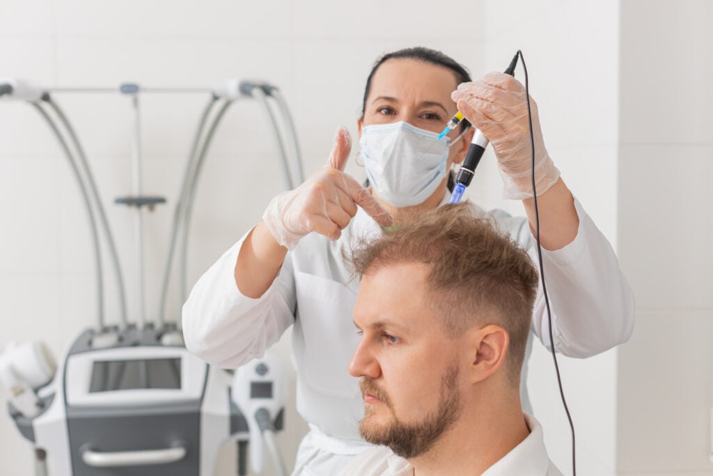 A doctor gives a thumbs up while performing exosome therapy on a man's scalp.