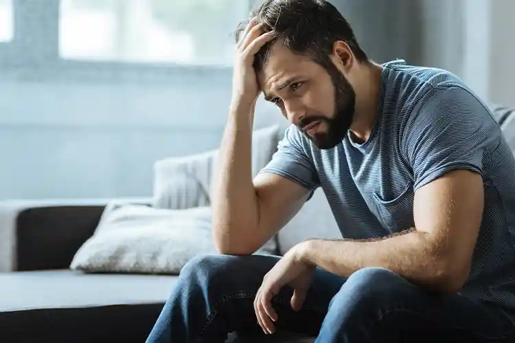 A man looks depressed, with his hand on his head and is visibly sad