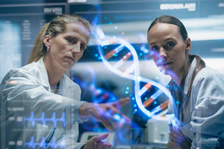 Two female scientists examine an onscreen illustration of a double helix.