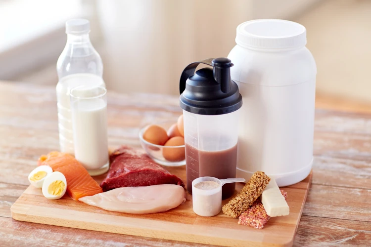 A collection of protein-rich food sources, including eggs, protein shakes, and chicken, gathered on a cutting board.