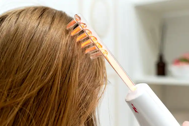A woman uses an electrical comb on her hair.