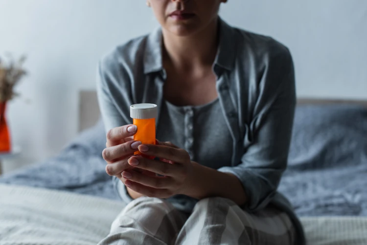 A menopausal woman holding a prescription pill bottle while sitting on her bed.