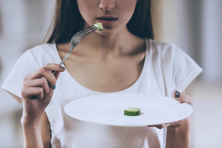 A concept shot of a woman contemplating taking a small bite of a single slice of cucumber.