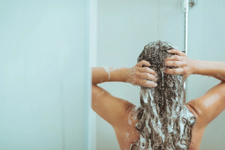 A woman washing shampoo out of her hair in the shower.