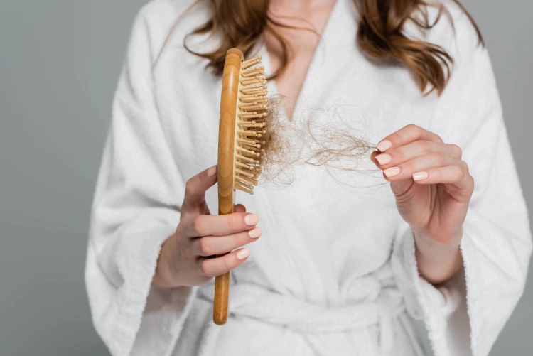 A cropped view of a woman pulling hair out of a hairbrush.