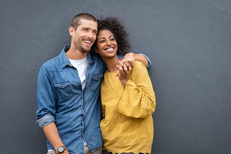 A man and woman have their arms around one another and are smiling.