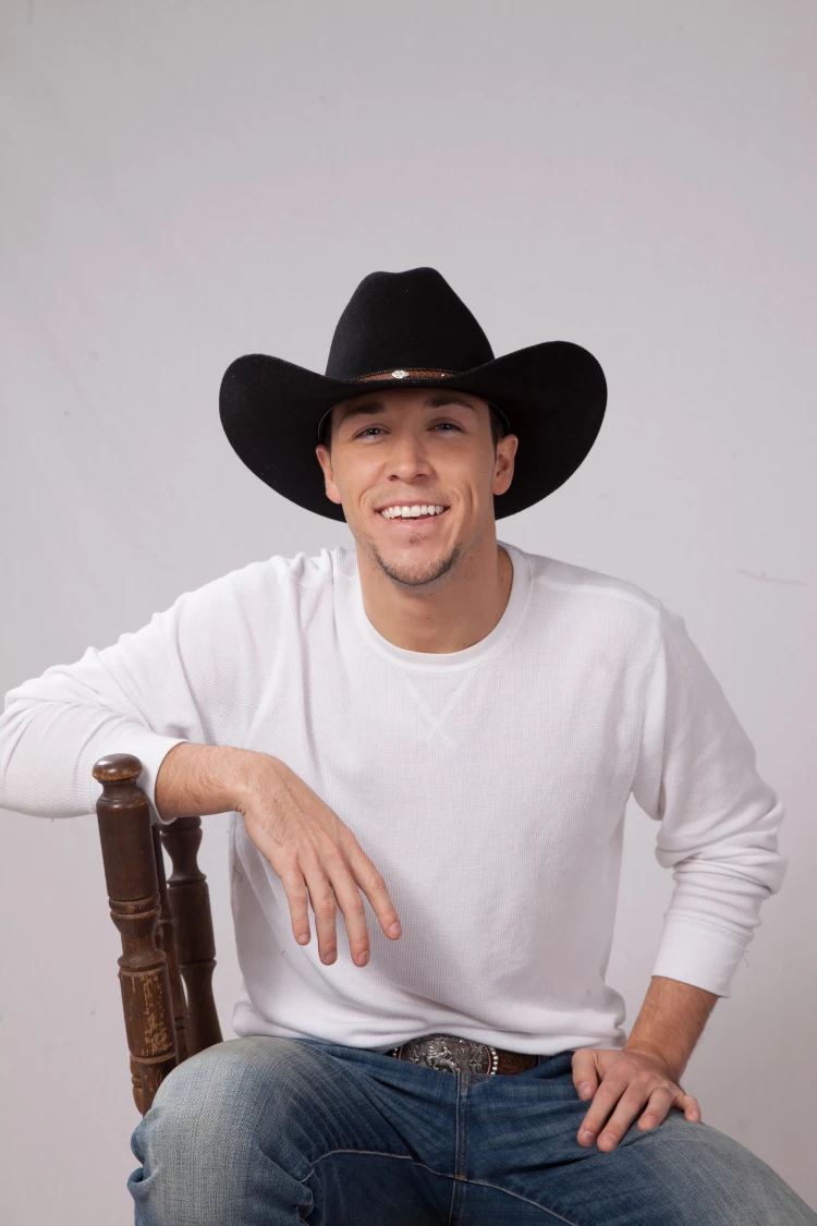 A happy man in a cowboy hat smiling and sitting on a chair.