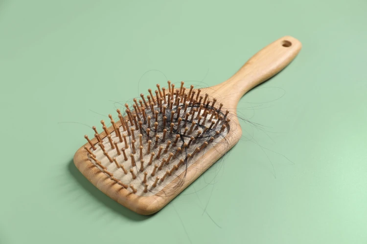A paddle brush with hair in the teeth lying on a green table. 