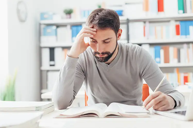 A bearded man studies, appearing stressed.