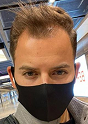 Man wearing a black face mask at an indoor location, with short styled hair and a focused expression.