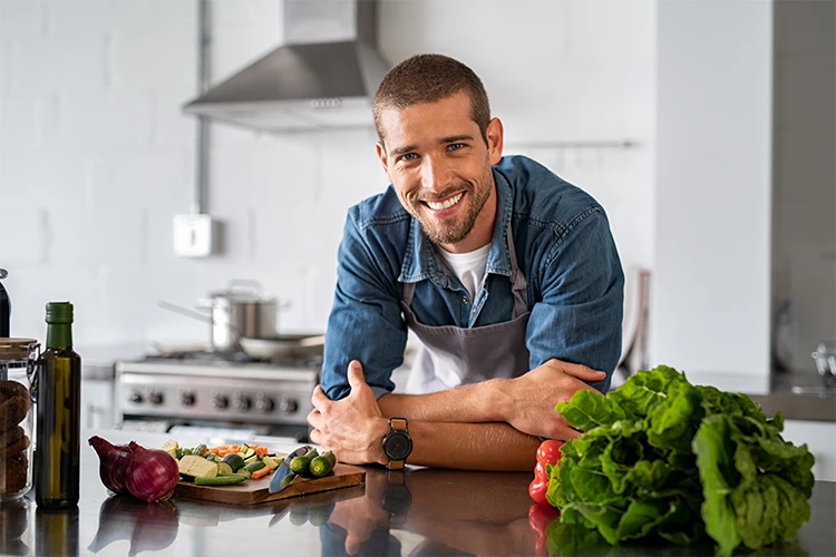 A smiling man in a kitchen full of fresh produce.