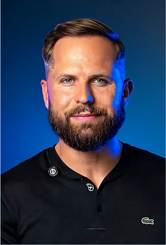 Man with short hair and beard smiling slightly, wearing a black shirt against a blue background.