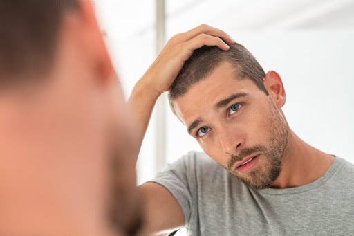 A man examines his hair loss in the mirror.