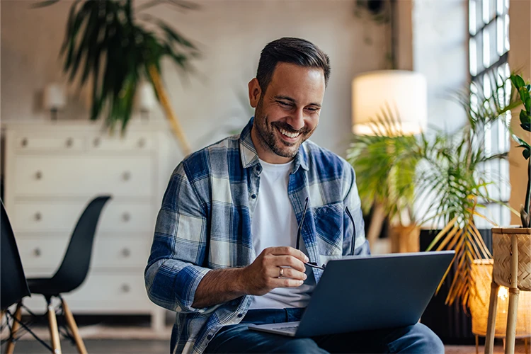 A man smiles while working on a laptop.