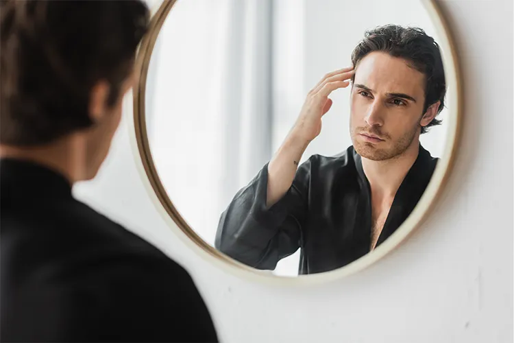 A man examines his hairline in the mirror.