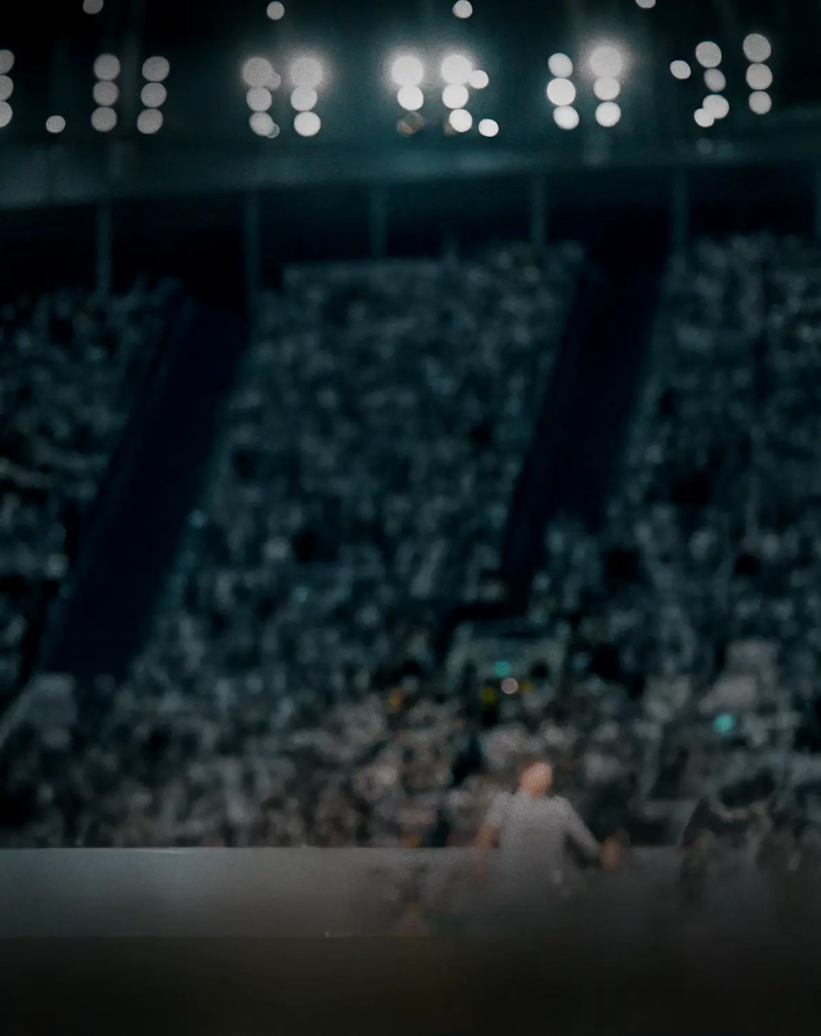 Blurred view of packed football stadium at night with bright floodlights and crowded stands