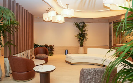 A modern lounge area in the Elitoria Hotel featuring a curved sofa, leather armchairs, and potted palms.