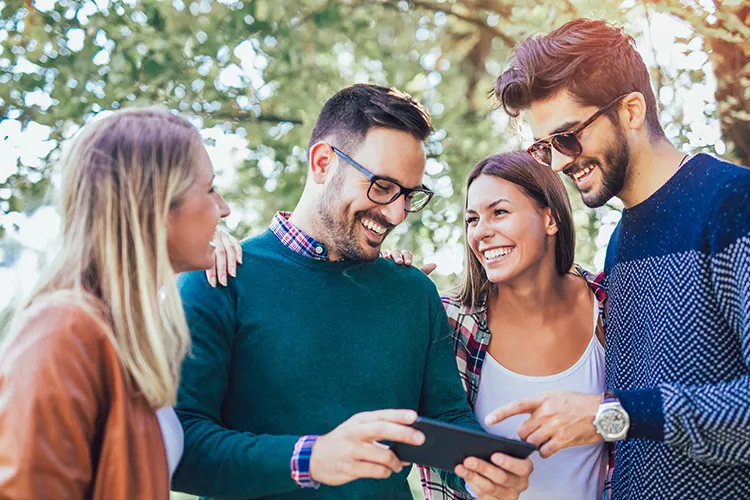 A group of people smile and lalugh while looking at something on a smartphone.