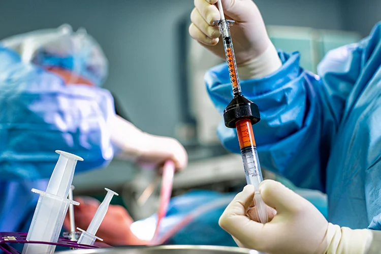 A surgeon holds a sample of fatty tissue they have extracted in a syringe.