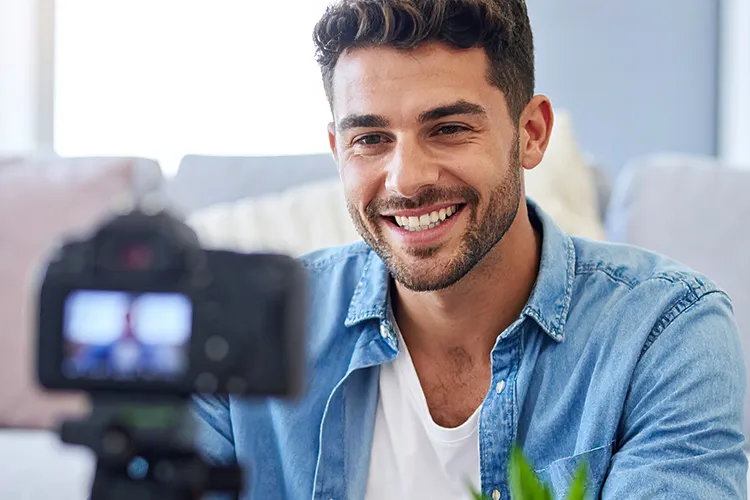 A young man smiles into a digital camera.
